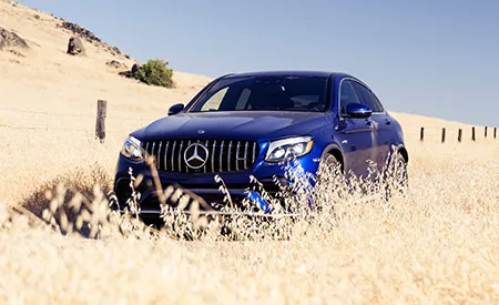 A blue Mercedes-Benz SUV drives through a field of wheat on a cloudless day.