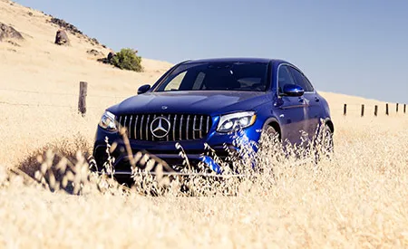 A blue Mercedes-Benz SUV drives through a field of wheat on a cloudless day. 